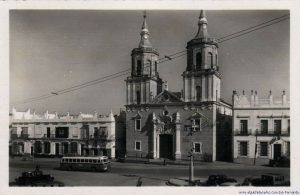 El Correo por la calle Real. Uno de los autobuses denominados "El Correo" a su paso por la calle Real pasando por delante de la Iglesia Mayor.Fotografía postal de San Fernando. Autor desconocido.